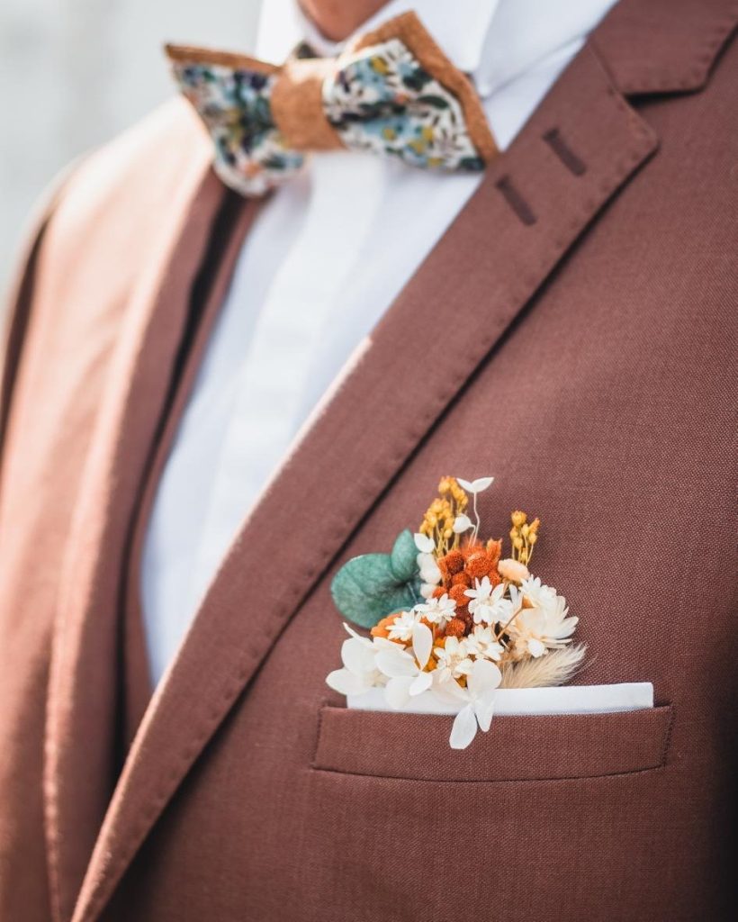 Détail de costume de marié rouille avec boutonnière en fleurs séchées orange, blanches et eucalyptus - Les pensées de Lily