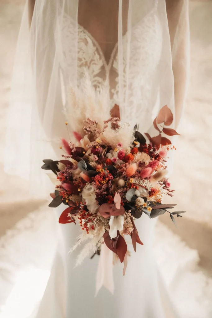 Bouquet en fleurs séchées aux couleurs chaudes tenu par une mariée en robe ivoire - Les pensées de Lily