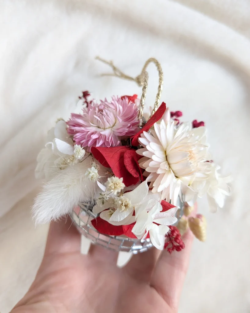 Boule miroir tenue à la main, garnie de fleurs séchées blanches, rouges et rose pastel - Les pensées de Lily
