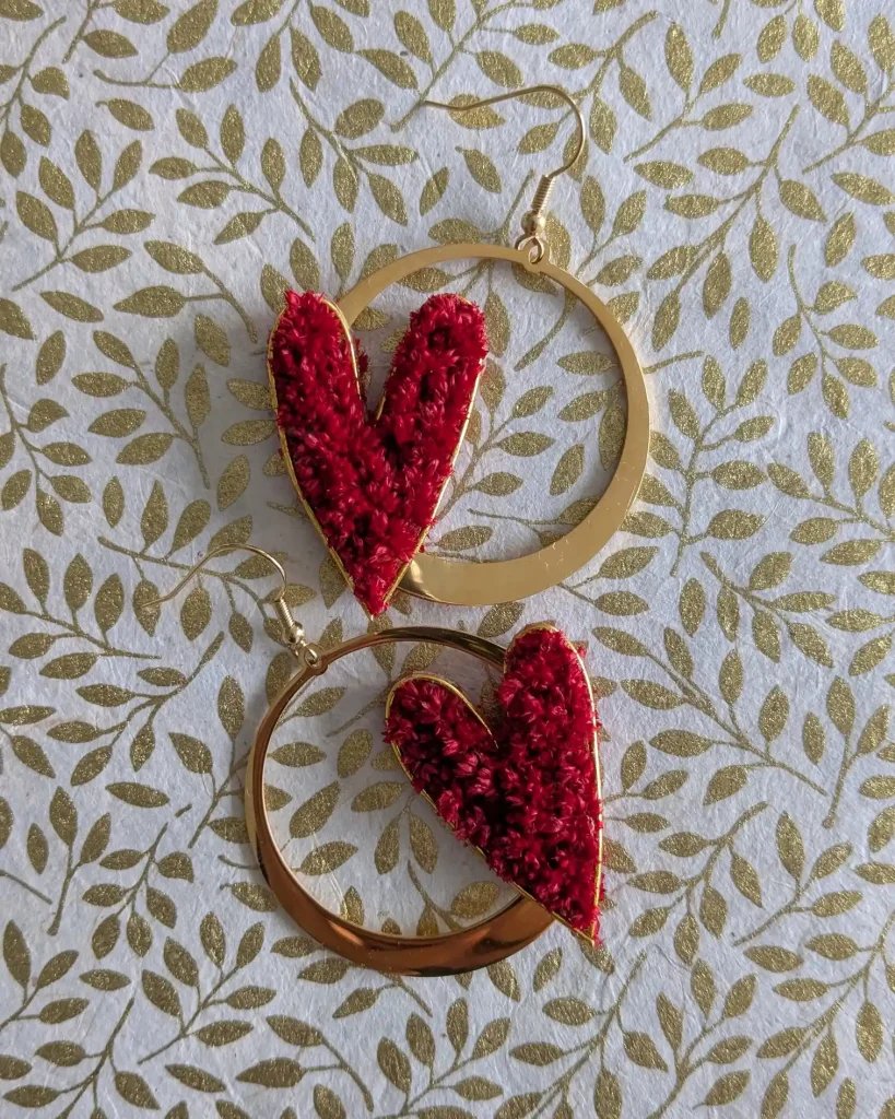 Boucles d’oreilles en forme de cœur rouge en fleurs séchées avec anneaux dorés martelés, posées à plat - Les pensées de Lily