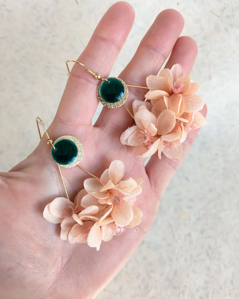 Boucles d’oreilles avec fleurs séchées pêche et pendentif rond vert émeraude, présentées dans une main – Les pensées de Lily