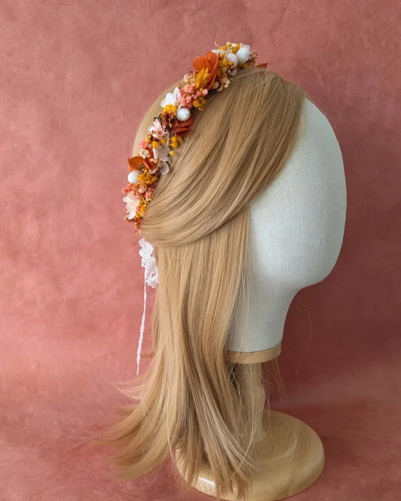 Couronne de tête en fleurs séchées oranges, jaunes et blanches, avec ruban de dentelle, présentée sur un mannequin devant un fond rosé – Les pensées de Lily