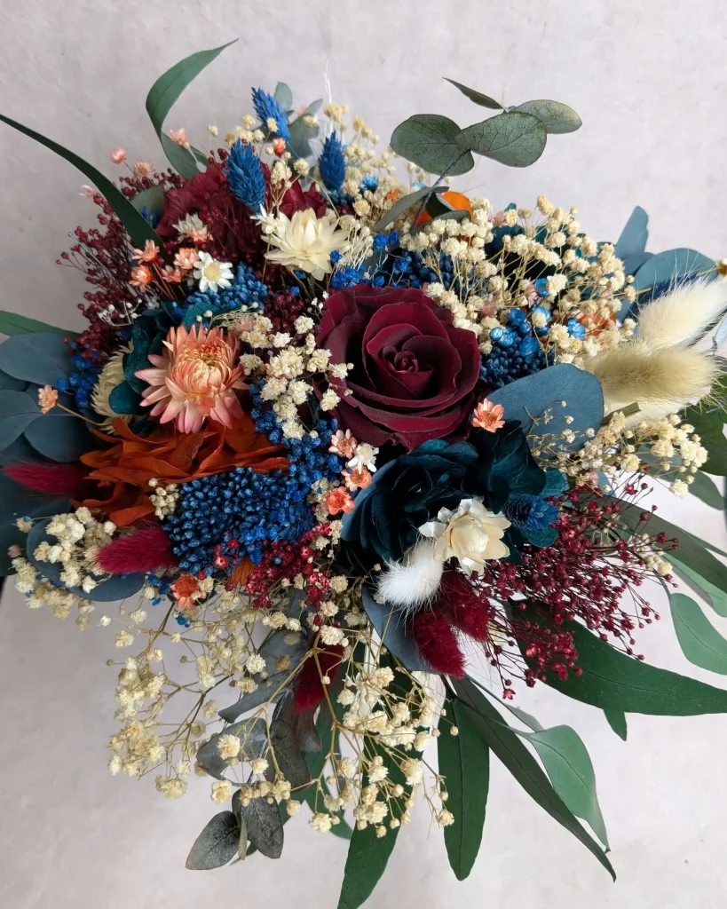 Bouquet de fleurs séchées bordeaux, bleu et crème dans un vase décoré de feuillages - Les pensées de Lily