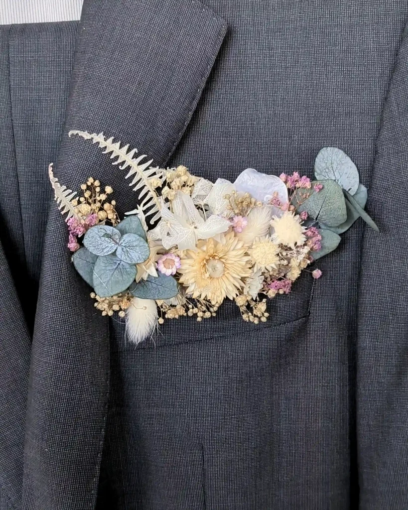 Poche de costume en fleurs séchées beige, vert et rose avec eucalyptus et dentelle, fixée sur veste grise - Les pensées de Lily