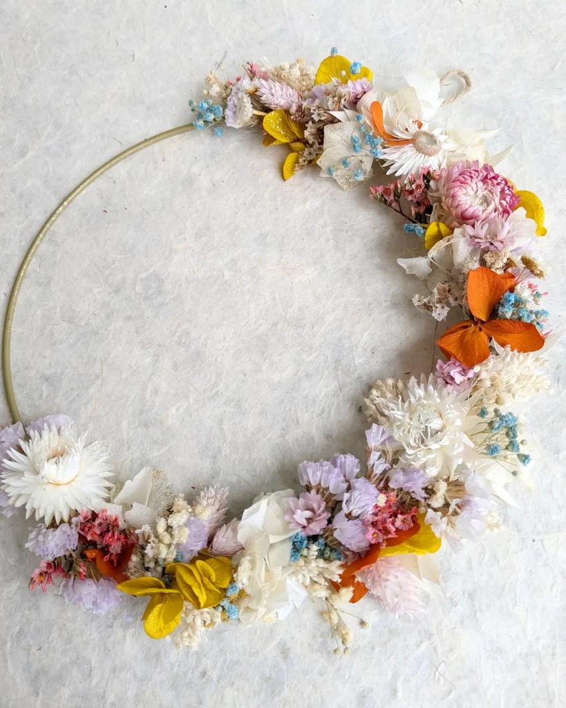 Couronne florale colorée en demi-cercle, ornée de fleurs séchées pastel, jaunes et orangées sur cercle métallique clair - Les pensées de Lily