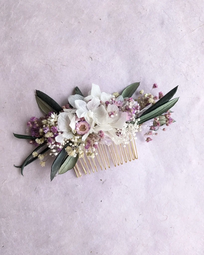 Peigne de cheveux orné de fleurs séchées blanches et lilas avec feuillage vert sur fond rose pâle - Les pensées de Lily