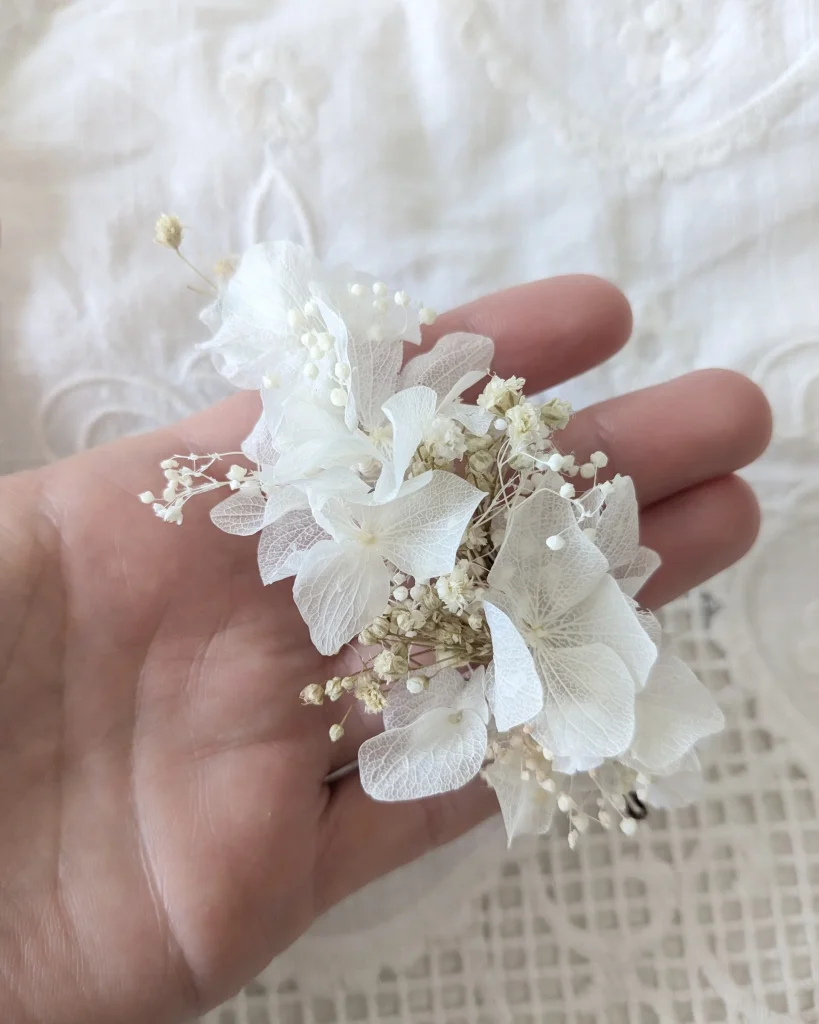 Peigne en fleurs séchées blanches tenu dans une main sur fond de tissu brodé – Les pensées de Lily