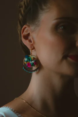 Gros plan sur une boucle d’oreille ronde garnie de fleurs séchées colorées portée par la mariée - Les pensées de Lily