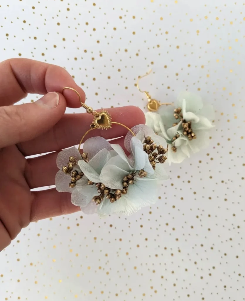 Boucles d’oreilles en fleurs séchées bleu ciel et baies dorées avec pendentif cœur doré tenu à la main - Les pensées de Lily