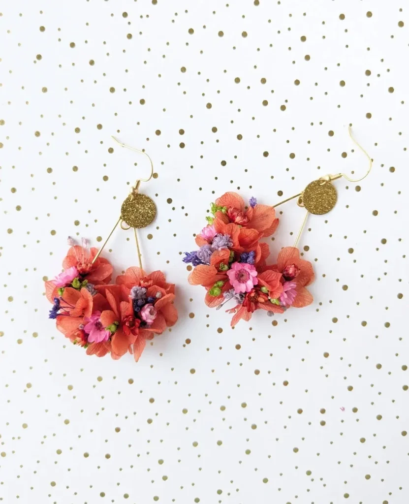 Boucles d’oreilles en fleurs séchées corail avec détails roses, violets et verts sur fond blanc à pois dorés - Les pensées de Lily
