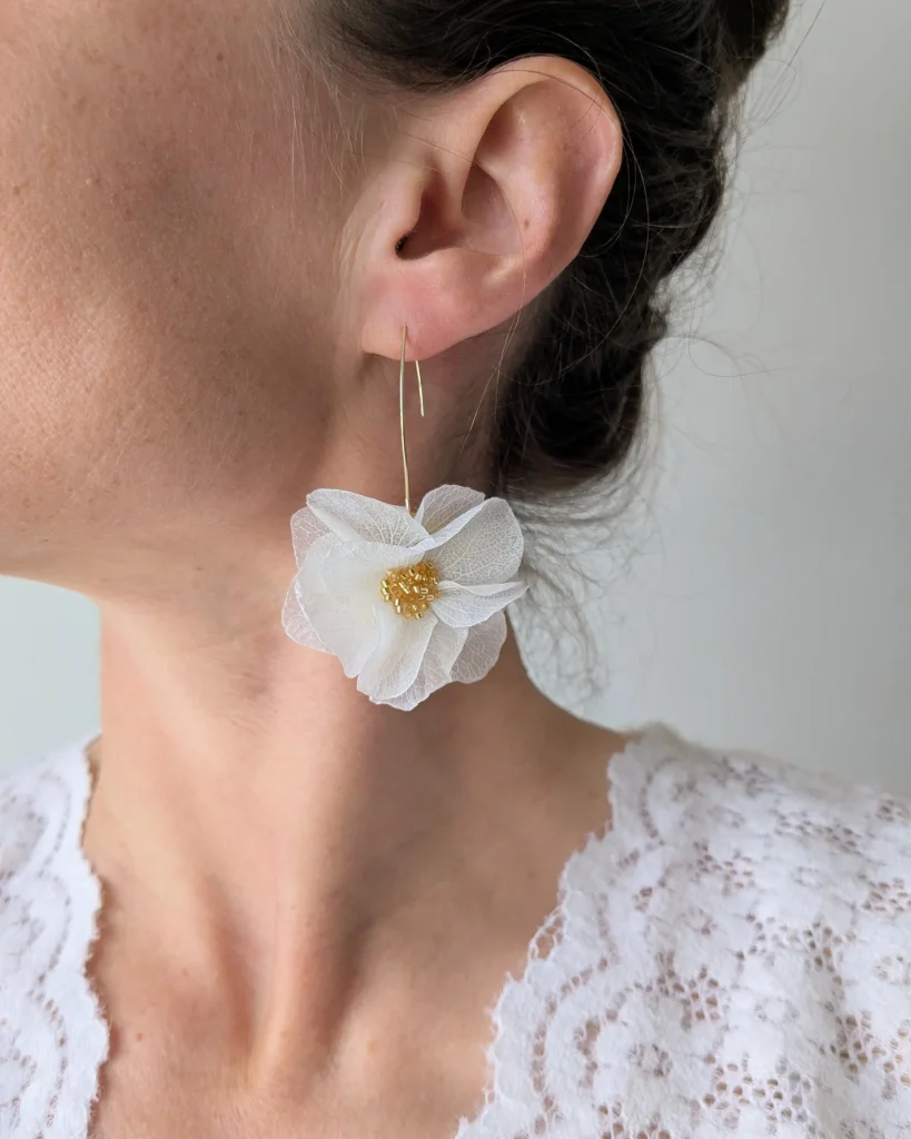 Boucle d’oreille fleur séchée blanche portée à l’oreille, monture fine dorée et tenue en dentelle – Les pensées de Lily