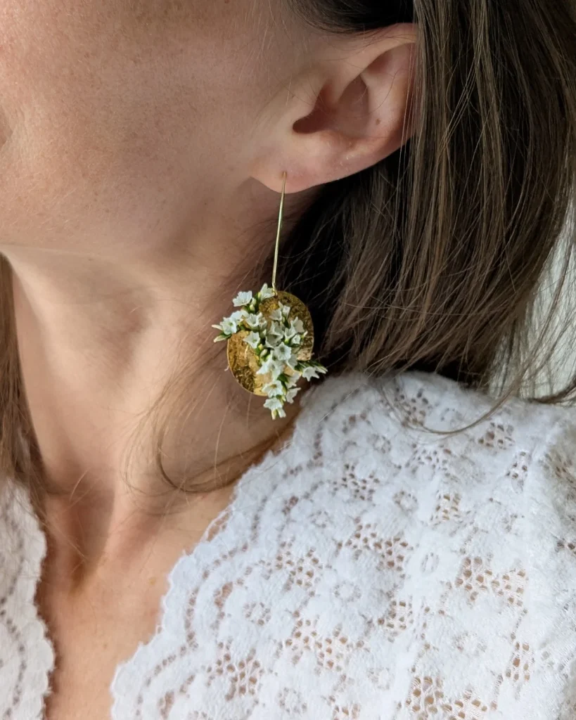 Boucles d’oreilles en fleurs séchées blanches et vertes sur pastille dorée martelée portées à l’oreille - Les pensées de Lily