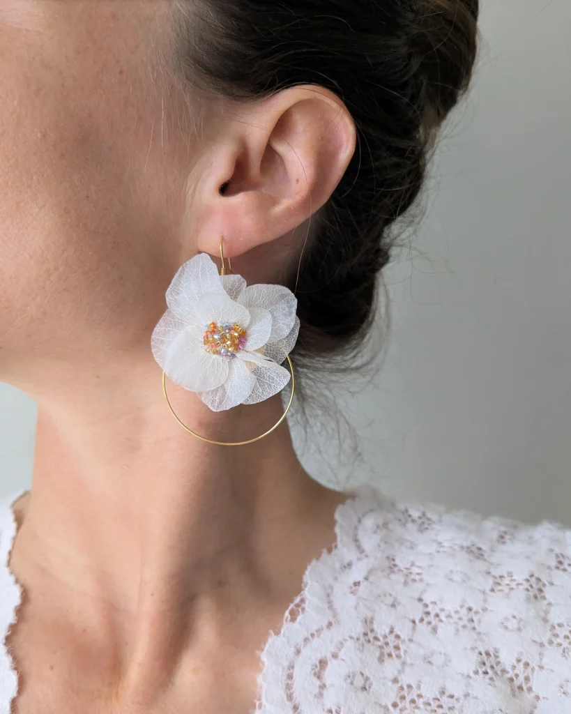 Boucle d’oreille fleur séchée blanche montée sur anneau doré, portée à l’oreille, cœur en perles irisées – Les pensées de Lily