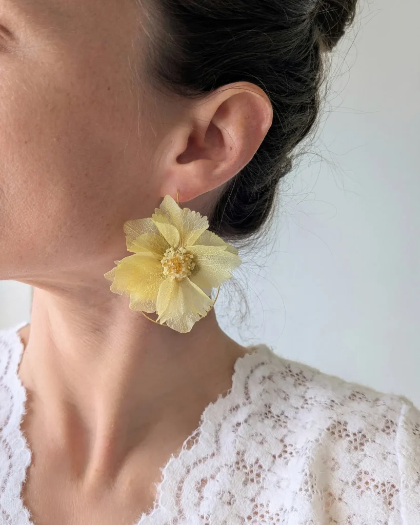 Boucle d’oreille en fleur séchée jaune montée sur anneau doré, portée à l’oreille avec haut en dentelle blanche – Les pensées de Lily