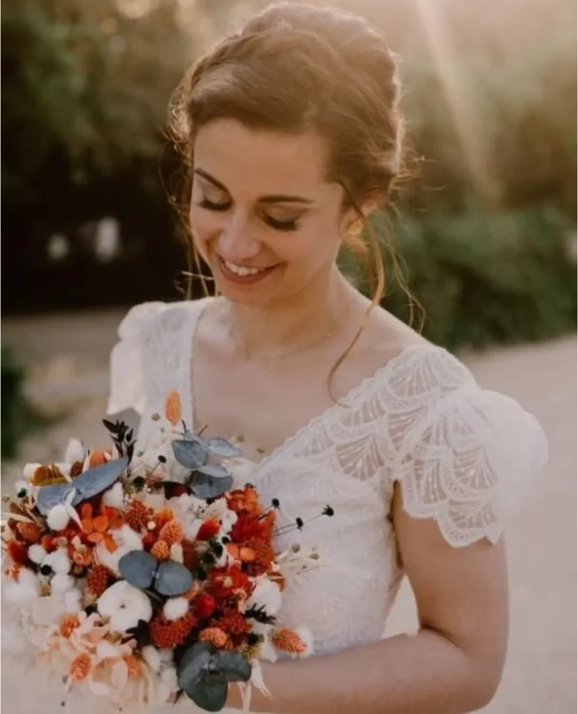 Mariée souriante tenant un bouquet de fleurs séchées aux teintes terracotta, blanc et eucalyptus - Les pensées de Lily