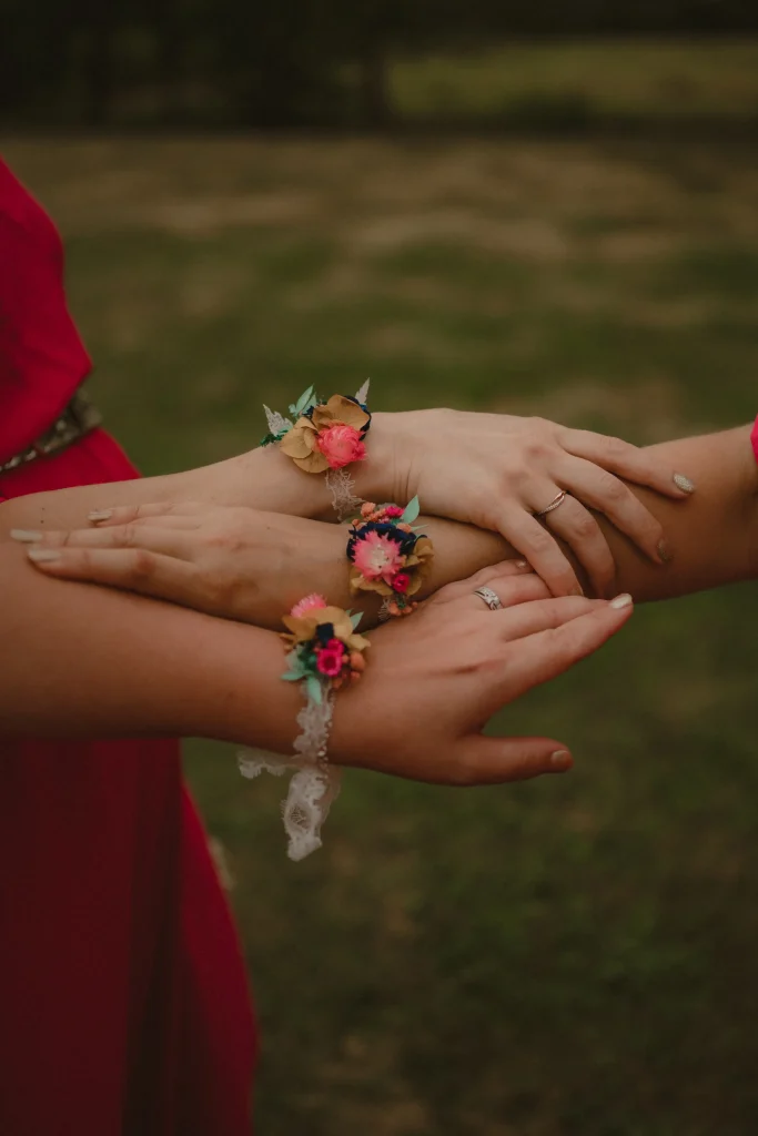 Mains entrelacées de femmes portant des bracelets en fleurs séchées lors d’un mariage champêtre - Les pensées de Lily