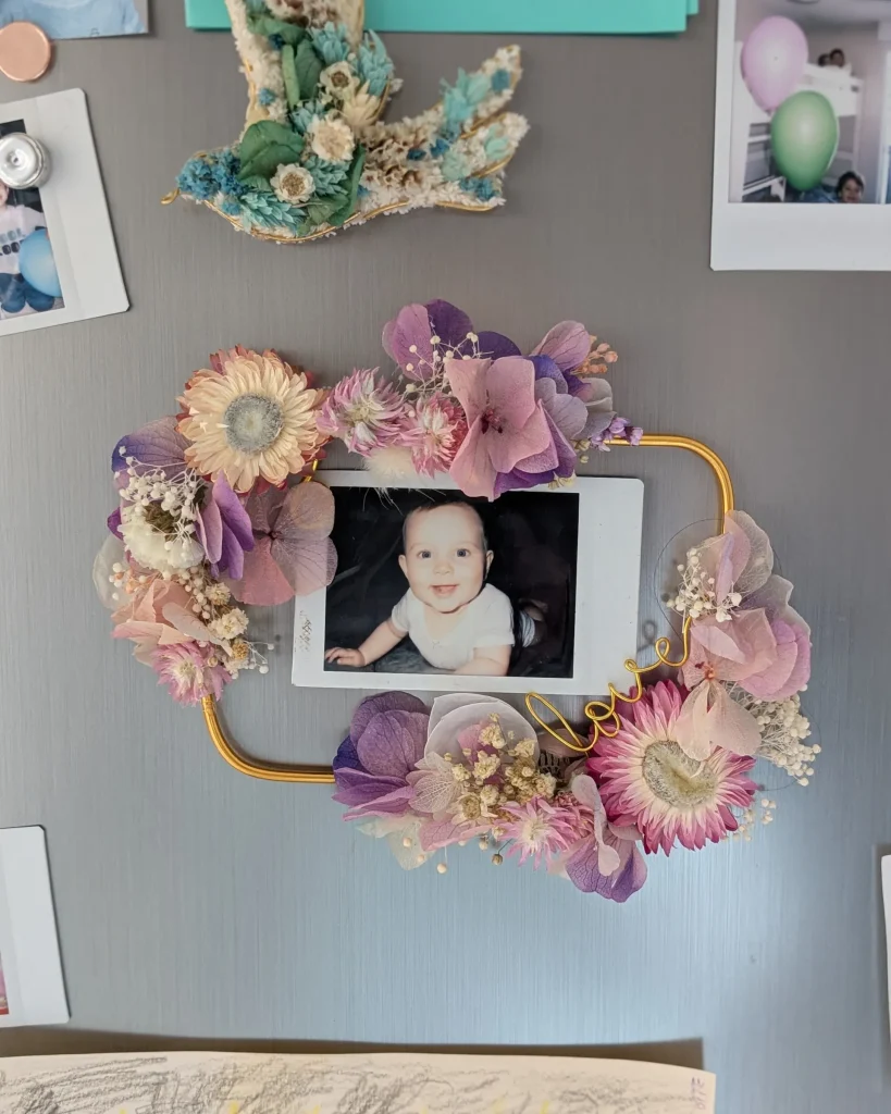 Cadre photo aimanté décoré de fleurs séchées dans les tons lilas, rose et blanc, fixé sur frigo avec photo d’un bébé - Les pensées de Lily