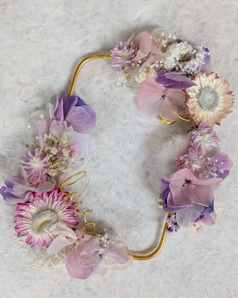 Cadre photo aimanté orné de fleurs séchées rose, mauve et lilas, avec armature dorée et fil "love", présenté sur fond naturel - Les pensées de Lily