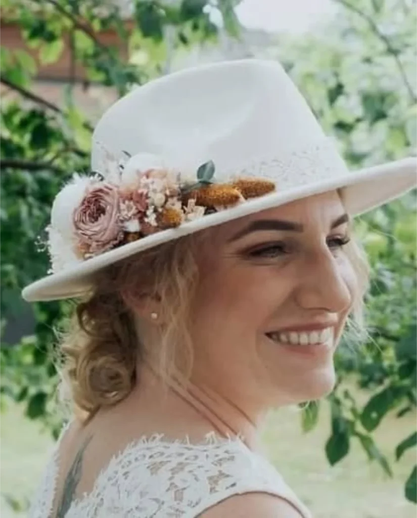 Mariée souriante portant un chapeau blanc orné de fleurs séchées rose poudré, beige et orangé - Les pensées de Lily