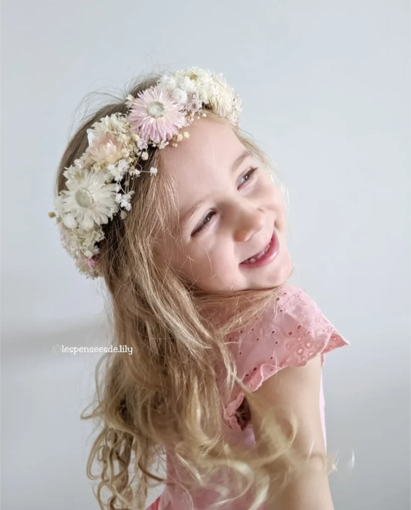Petite fille blonde souriante portant une couronne de fleurs séchées rose pâle et blanc sur cheveux lâchés - Les pensées de Lily