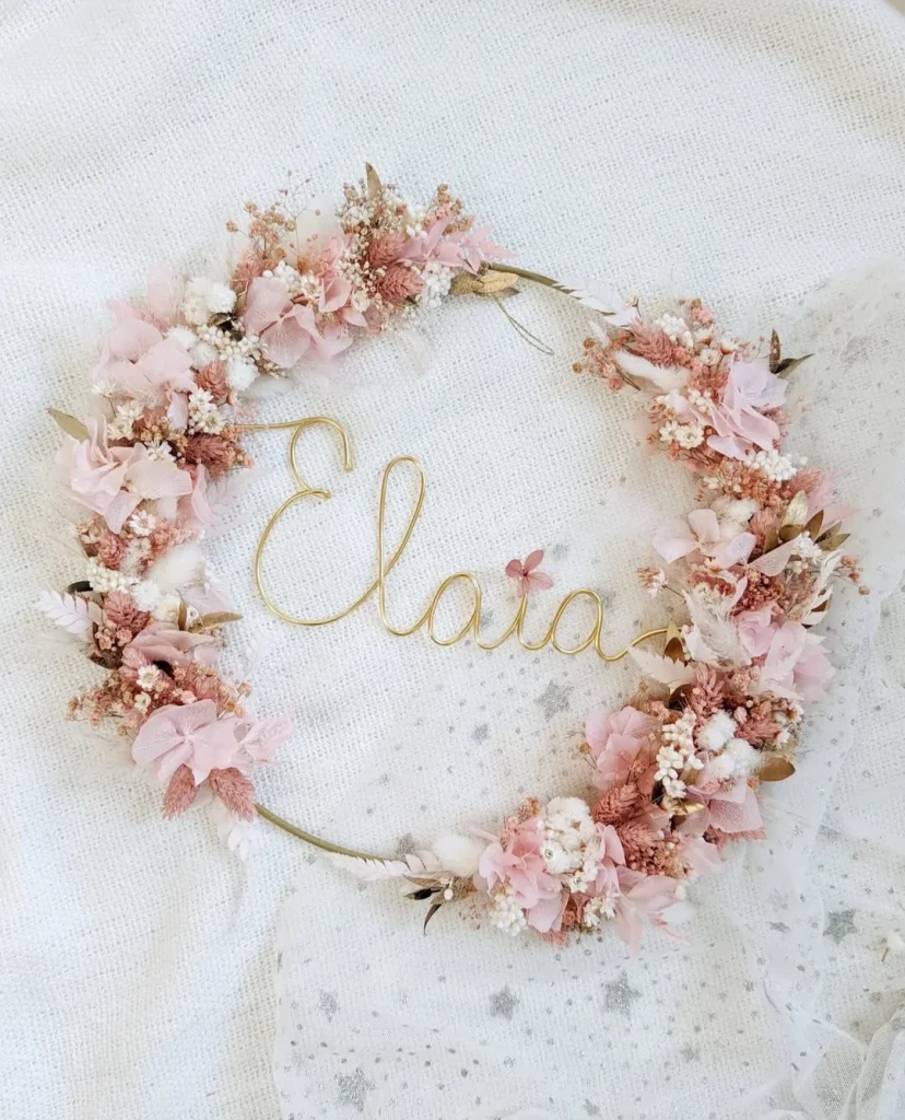 Couronne murale en fleurs séchées tons rose poudré et blanc, prénom Elaia en fil doré, posée sur tissu étoilé - Les pensées de Lily