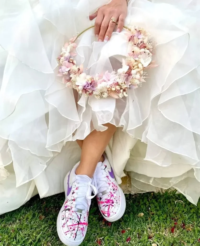 Mariée assise en robe blanche, baskets colorées aux pieds, tenant une couronne de fleurs séchées rose, beige et violet - Les pensées de Lily