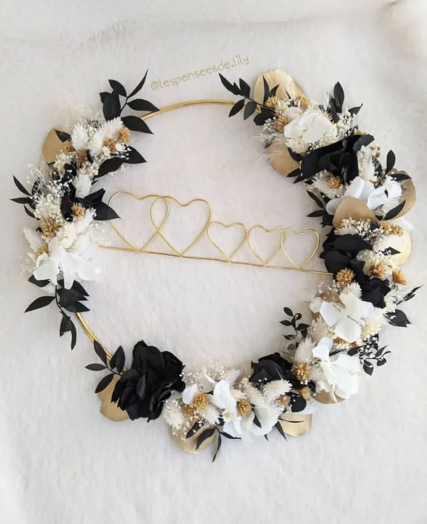 Couronne murale décorative avec cœurs entrelacés en fil doré, ornée de fleurs séchées noires, blanches, dorées et feuillage - Les pensées de Lily
