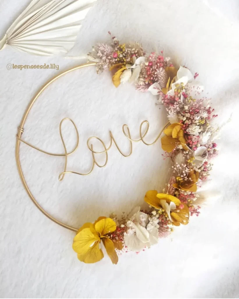 Couronne murale décorative avec le mot Love en fil doré, ornée de fleurs séchées blanches, jaunes et touches de rose - Les pensées de Lily