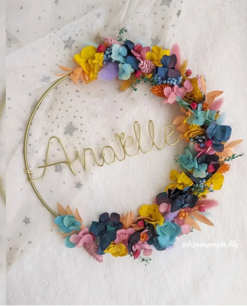 Couronne murale avec le prénom Anaëlle en fil doré, décorée de fleurs séchées bleu marine, turquoise, rose, jaune et orange sur fond étoilé - Les pensées de Lily