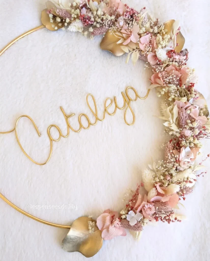 Couronne murale personnalisée avec le prénom Cataleya en fil doré, ornée de fleurs séchées ivoire, rose nude et feuillage doré sur fond doux - Les pensées de Lily