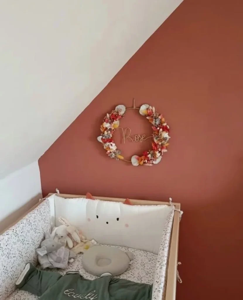 Couronne murale en fleurs séchées rouges et orangées avec prénom Rose au fil doré, accrochée dans une chambre de bébé aux murs terracotta - Les pensées de Lily