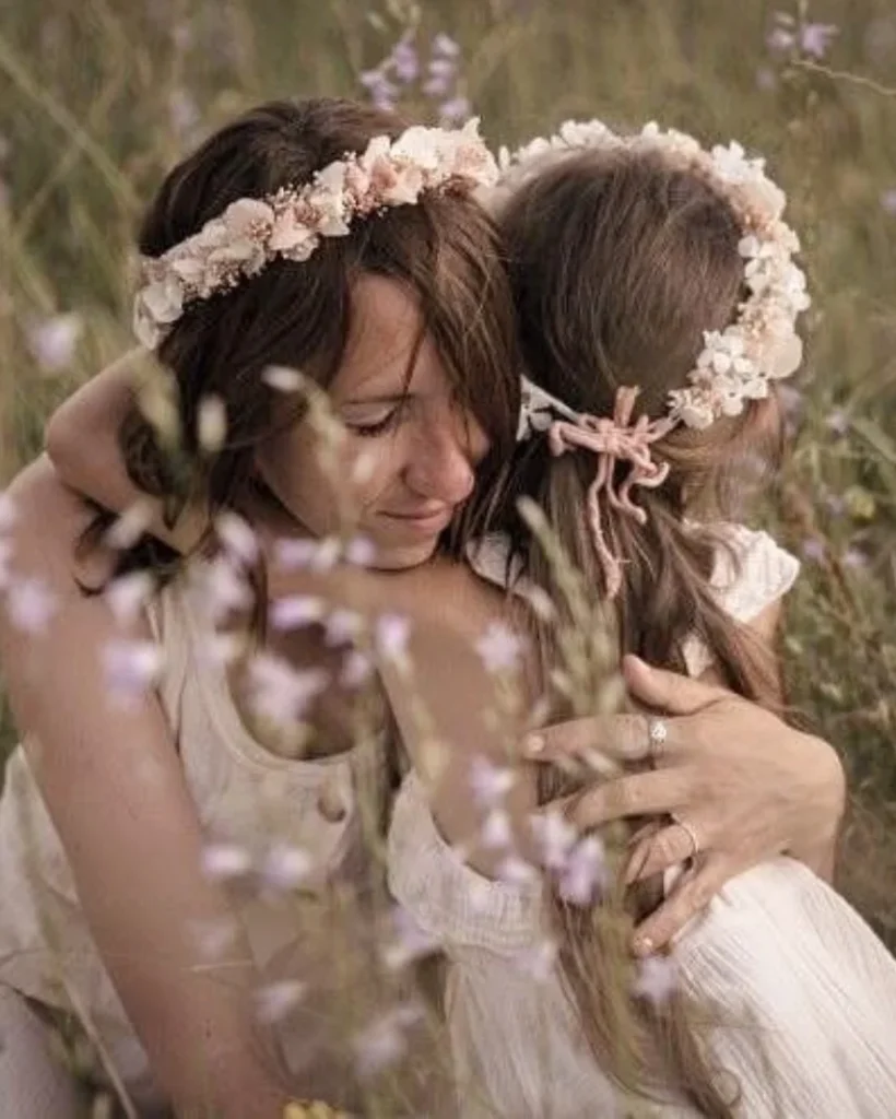 Maman et fillette portant des couronnes de fleurs séchées blanc et rose, enlacées tendrement dans un champ fleuri - Les pensées de Lily