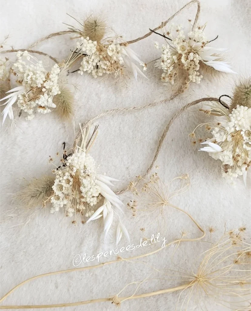 Guirlande en ficelle de jute ornée de petits bouquets de fleurs séchées blanches et beiges, présentée sur fond en tissu doux – Les pensées de Lily