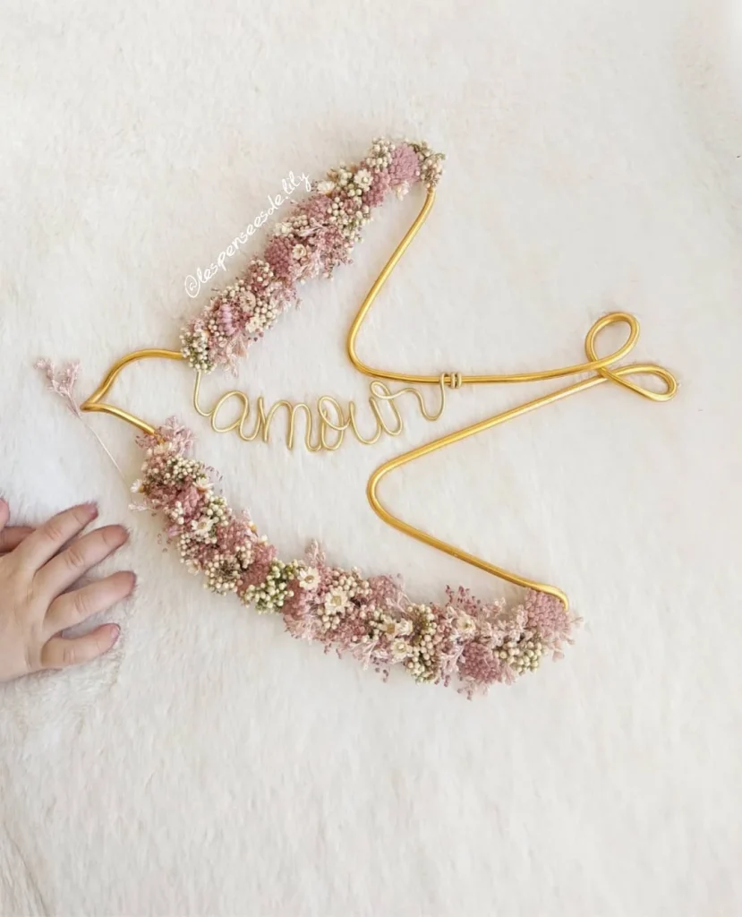 Décoration en fil doré en forme d’hirondelle, ornée de fleurs séchées roses et blanches, avec le mot « amour » intégré – Les pensées de Lily