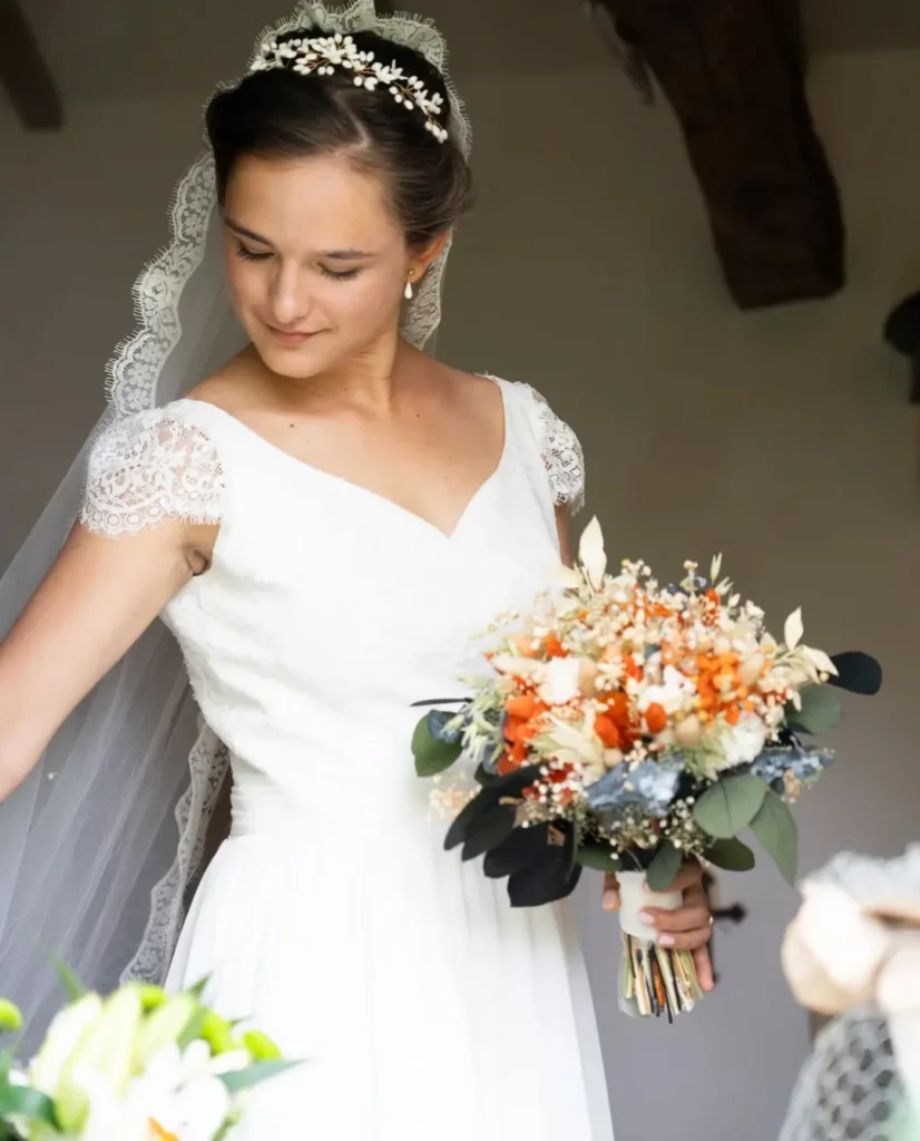 Jeune mariée en robe blanche avec un bouquet de fleurs séchées aux teintes terracotta, beige et feuillage vert foncé - Les pensées de Lily