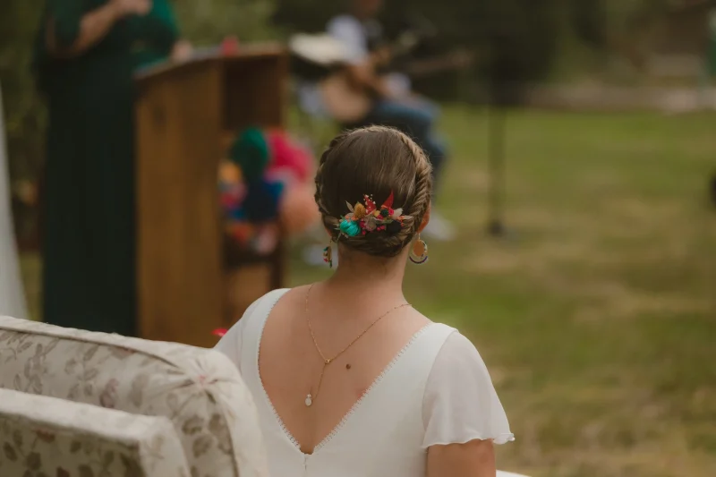 Mariée assise de dos, coiffure tressée ornée de fleurs séchées colorées, lors d’un mariage en plein air - Les pensées de Lily