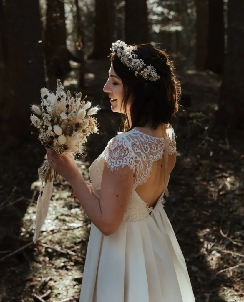 Mariée en robe ivoire tenant un bouquet de fleurs séchées blanches et noires, couronne assortie dans les cheveux, en pleine forêt - Les pensées de Lily