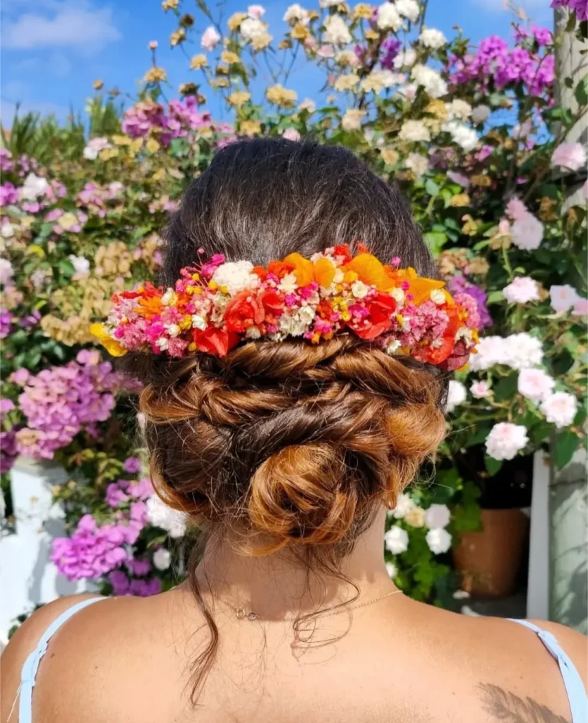 Peigne floral en fleurs séchées orange, rose, rouge et jaune porté dans un chignon tressé devant un mur de fleurs - Les pensées de Lily